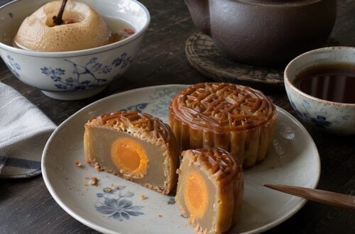 Aufgeschnittene Mondkuchen mit Lotuspaste und Eigelb neben einer gedämpften Birne und einer Teekanne