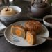 Aufgeschnittene Mondkuchen mit Lotuspaste und Eigelb neben einer gedämpften Birne und einer Teekanne